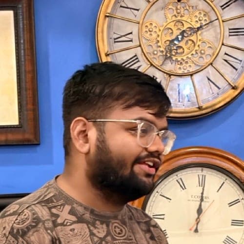 Ayush Shah mid-conversation in front of a blue wall with vintage clocks